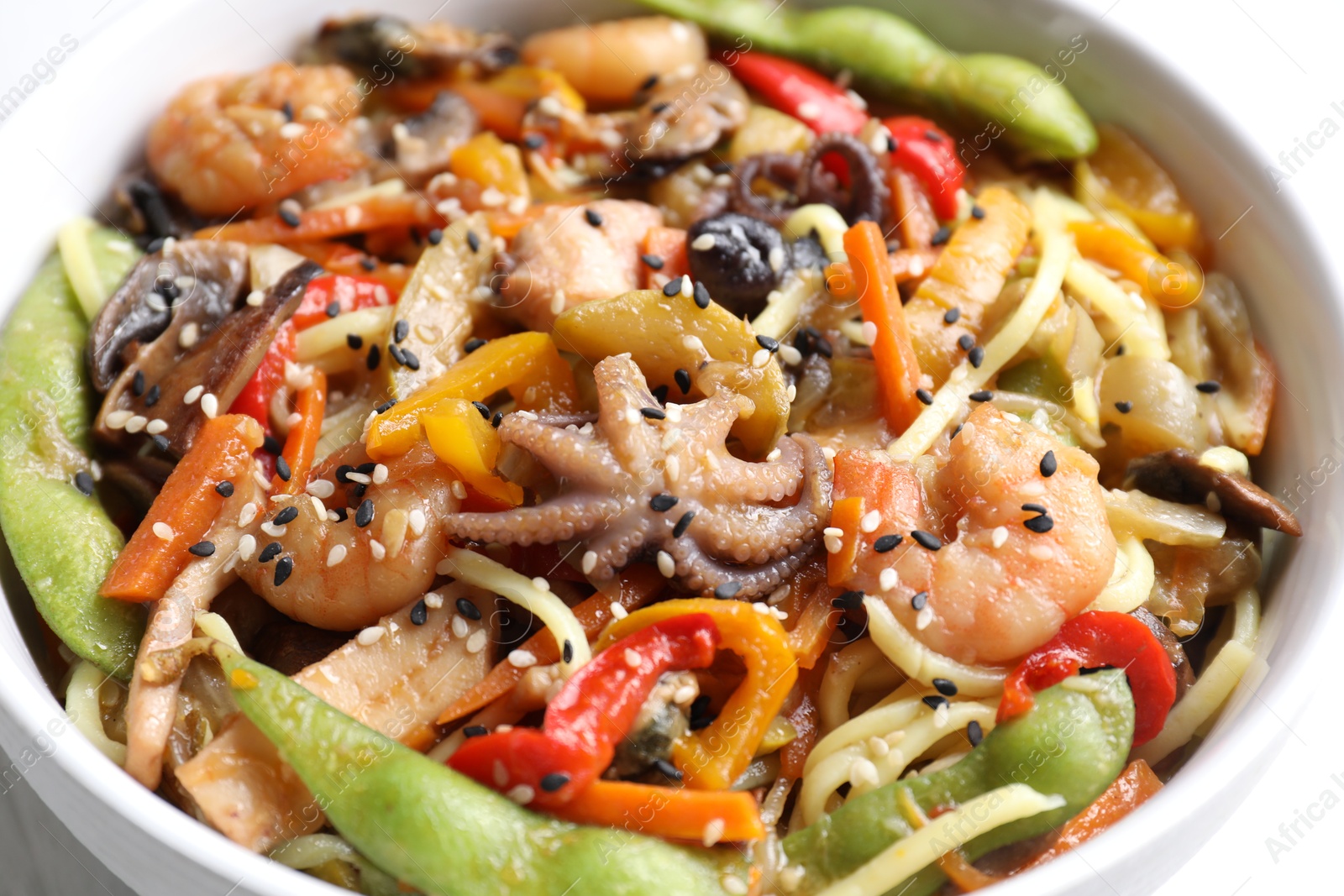 Photo of Stir-fry noodles with sea food in bowl on white table, closeup