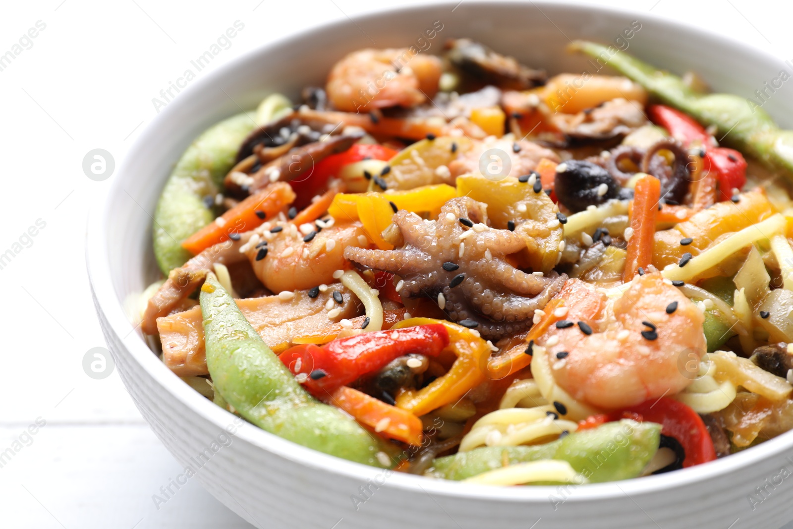 Photo of Stir-fry noodles with sea food in bowl on white table, closeup