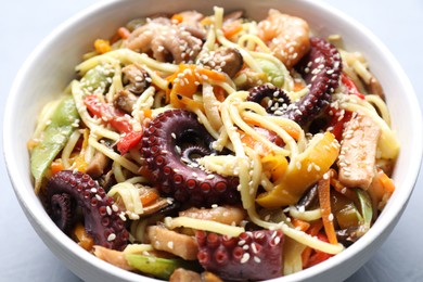 Photo of Stir-fry noodles with sea food in bowl on light grey table, closeup