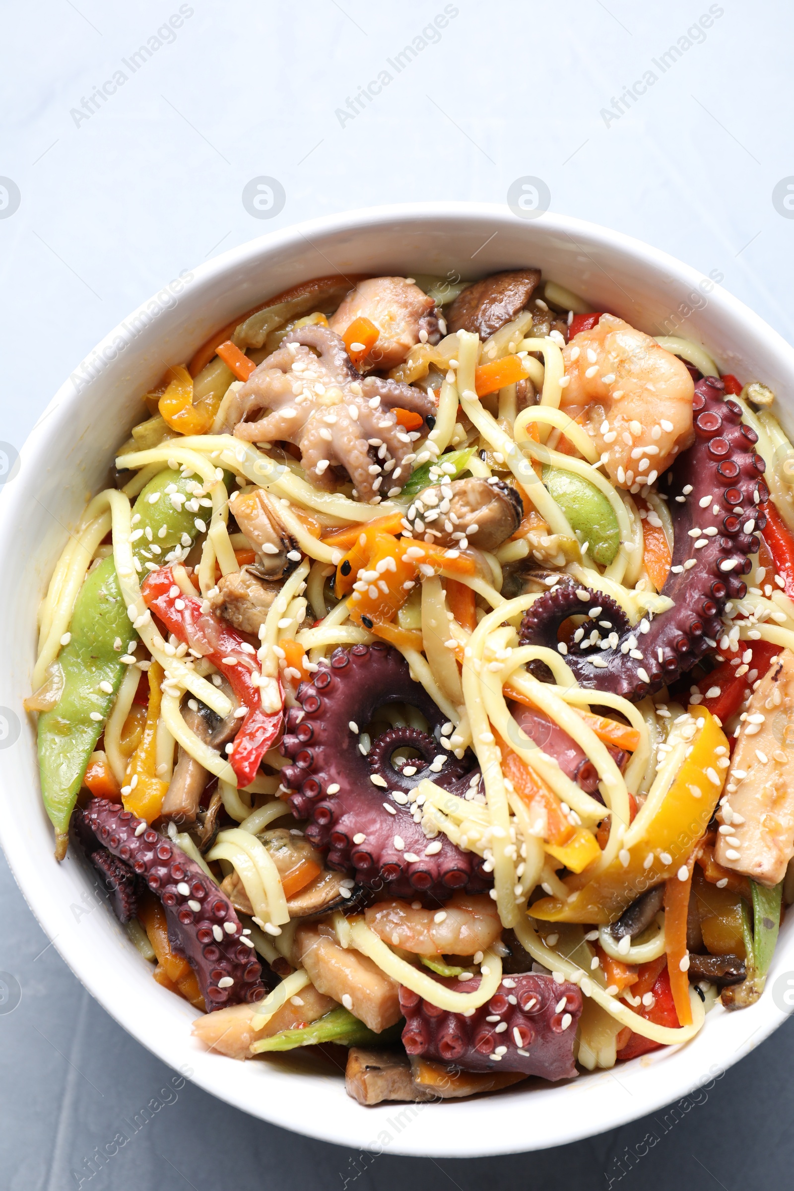 Photo of Stir-fry noodles with sea food in bowl on light grey table, top view