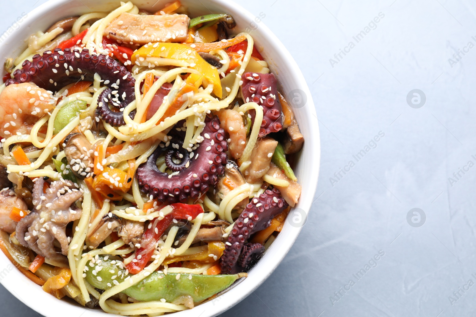 Photo of Stir-fry noodles with sea food in bowl on light grey table, top view. Space for text