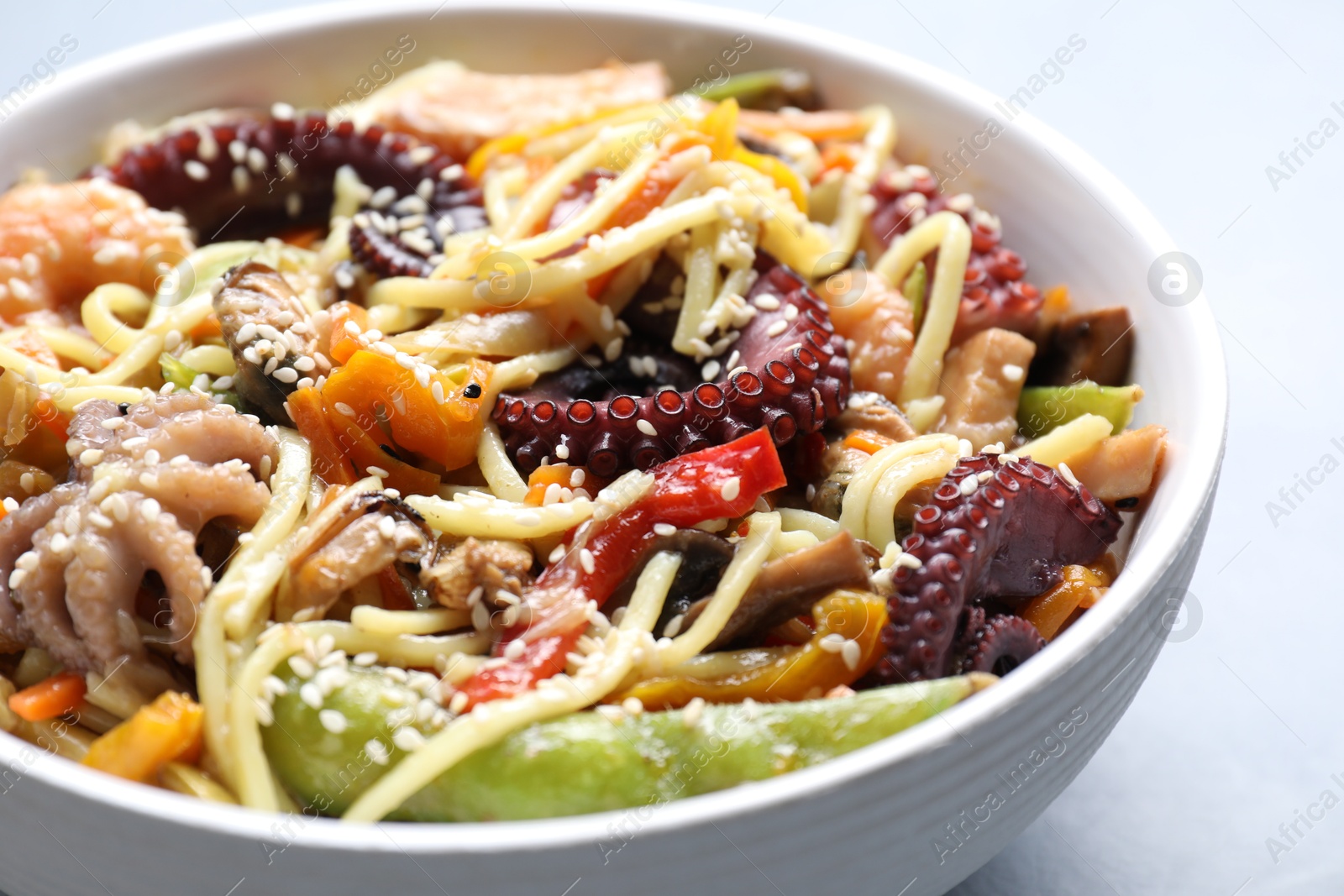 Photo of Stir-fry noodles with sea food in bowl on light grey table, closeup