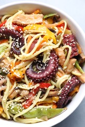 Stir-fry noodles with sea food in bowl on light grey table, top view