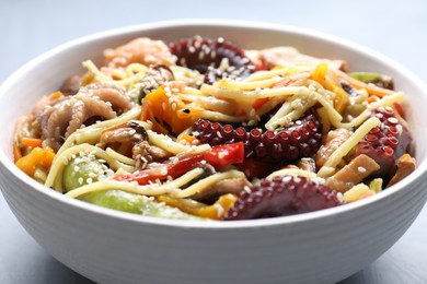 Photo of Stir-fry noodles with sea food in bowl on light grey table, closeup