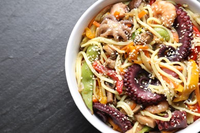 Stir-fry noodles with sea food in bowl on grey textured table, top view. Space for text