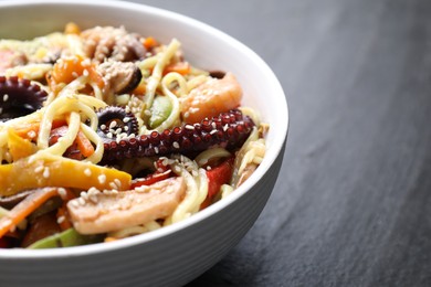 Photo of Stir-fry noodles with sea food in bowl on grey textured table, closeup. Space for text