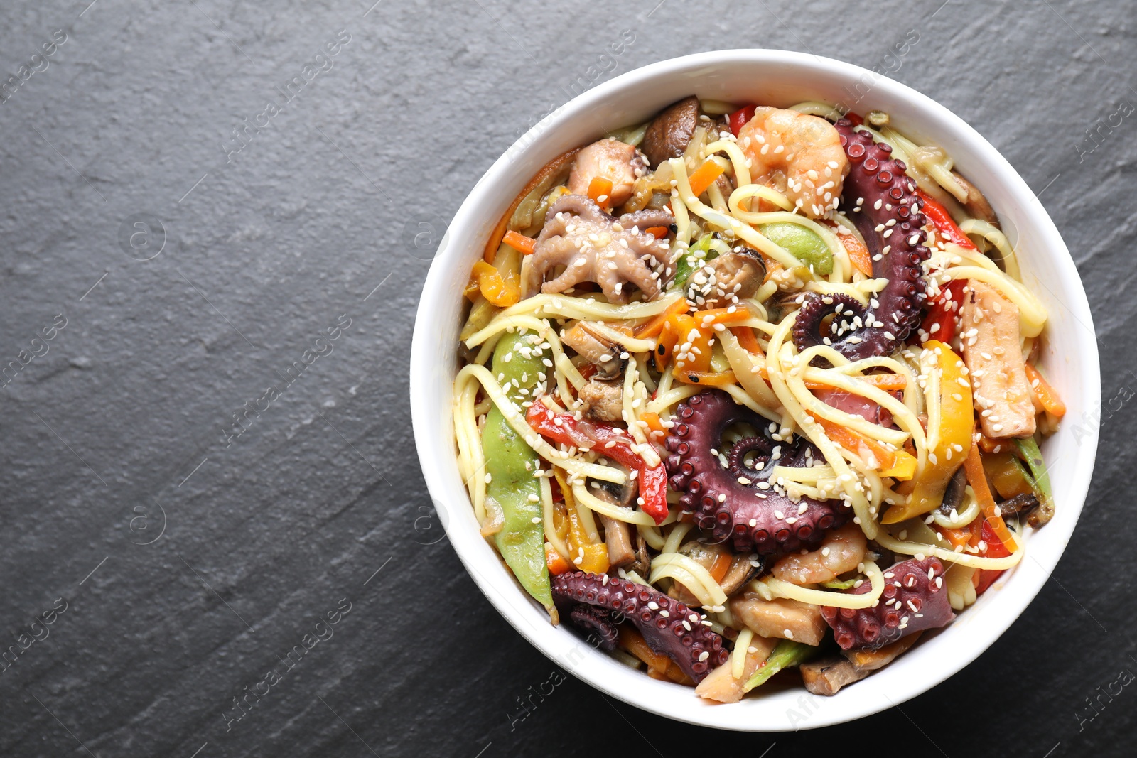 Photo of Stir-fry noodles with sea food in bowl on grey textured table, top view. Space for text