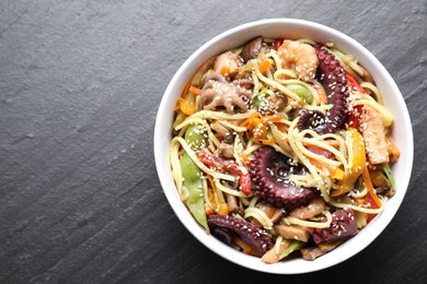 Stir-fry noodles with sea food in bowl on grey textured table, top view. Space for text