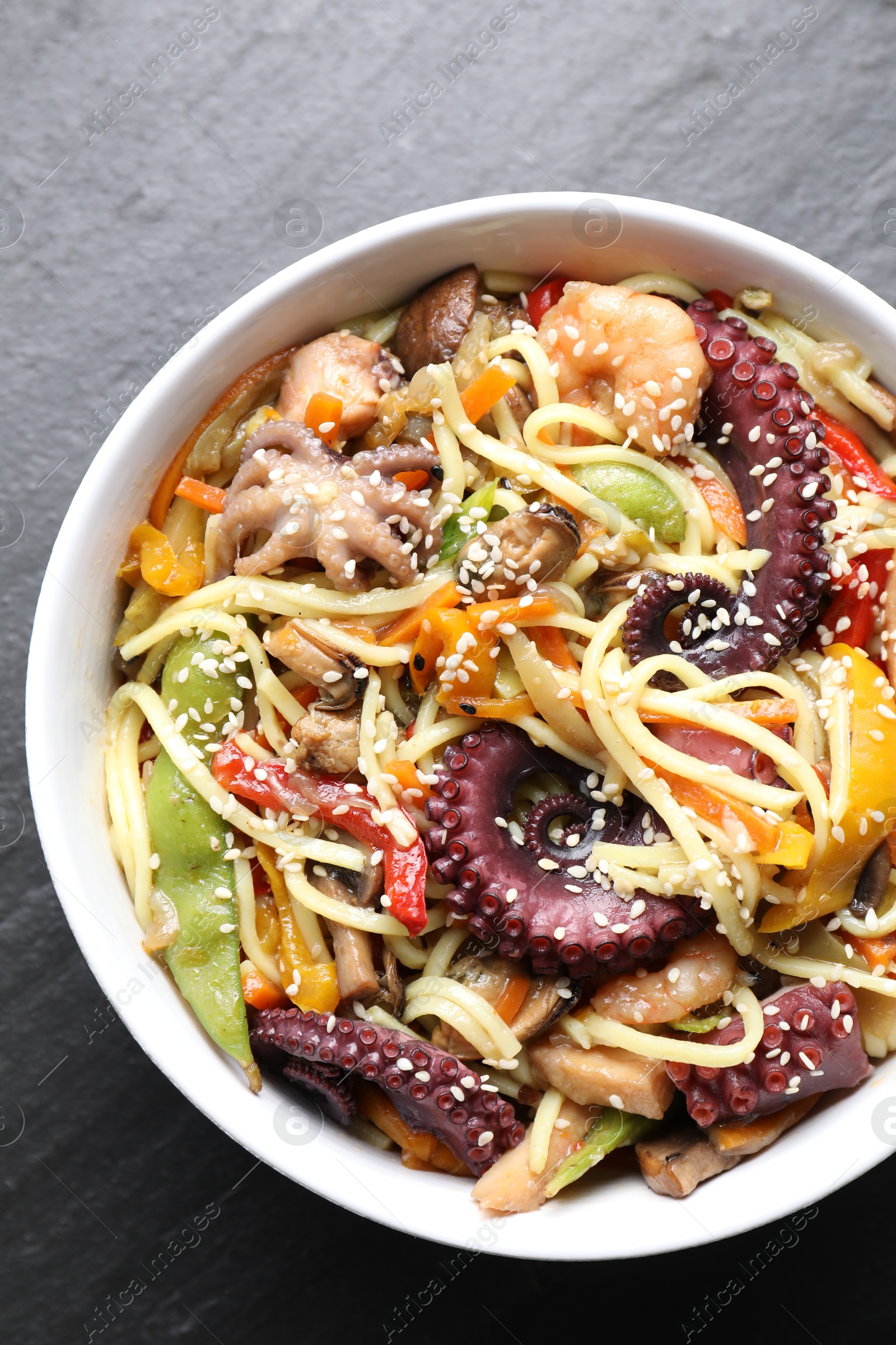 Photo of Stir-fry noodles with sea food in bowl on grey textured table, top view