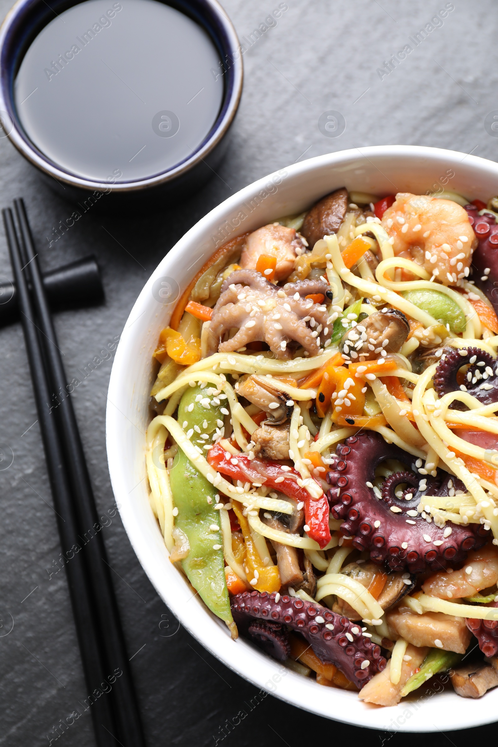 Photo of Stir-fry noodles with sea food served on grey textured table, flat lay