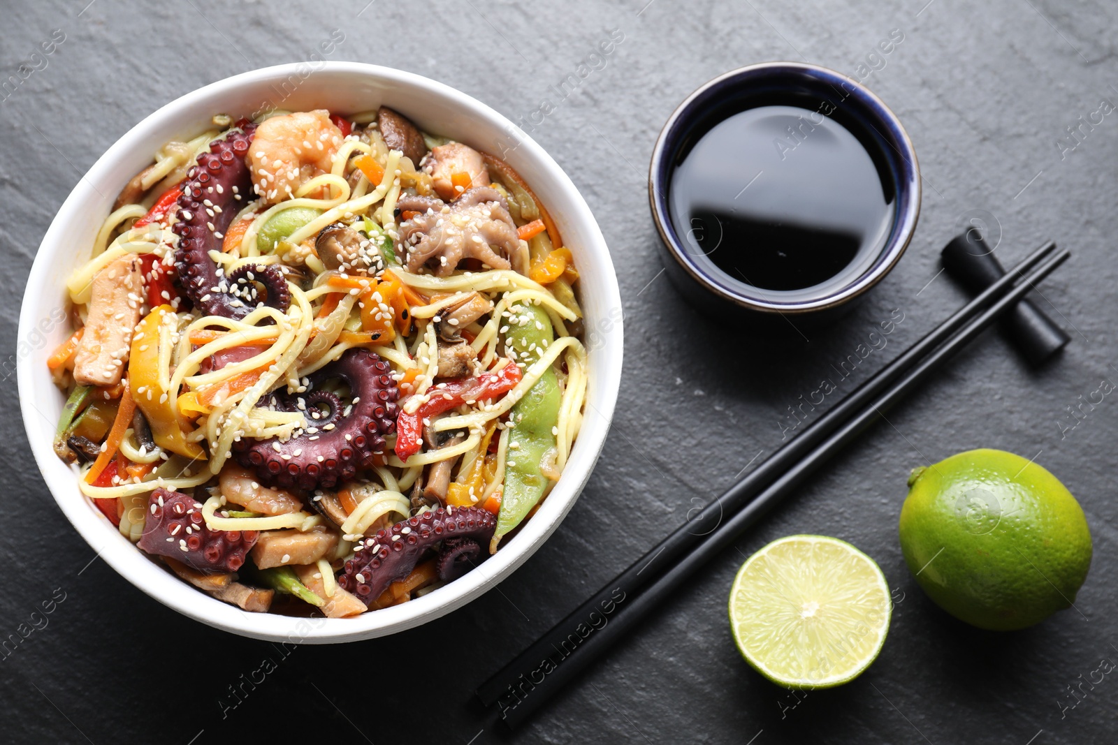 Photo of Stir-fry noodles with sea food served on grey textured table, flat lay