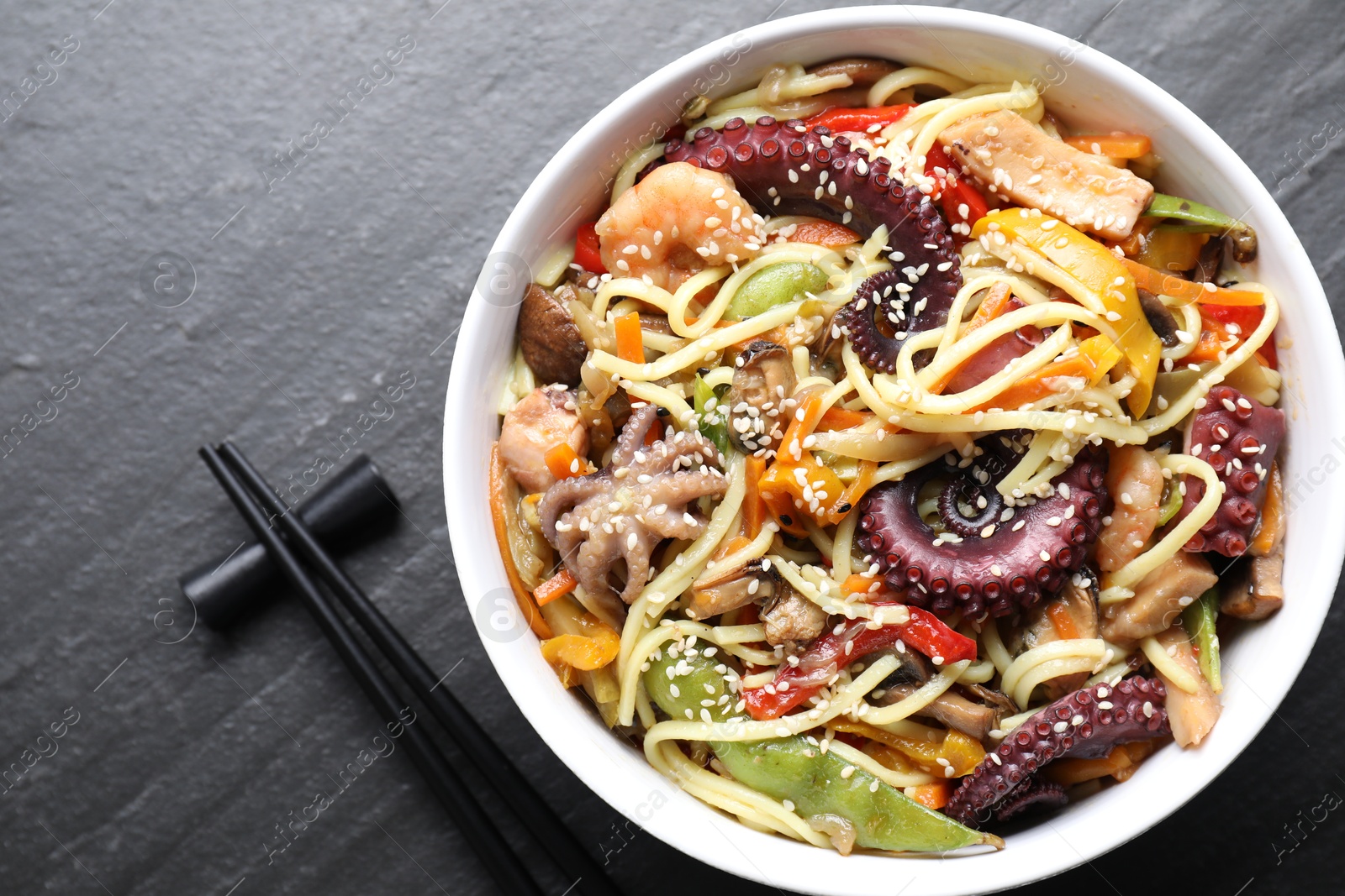 Photo of Stir-fry noodles with sea food served on grey textured table, flat lay