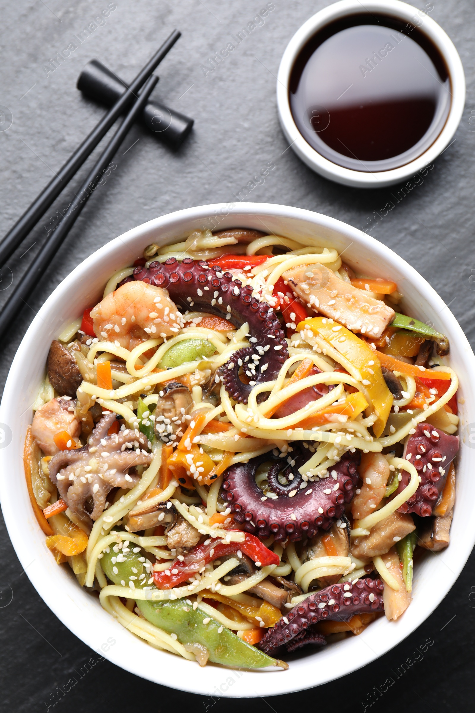 Photo of Stir-fry noodles with sea food served on grey textured table, flat lay