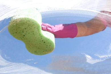 Woman washing window with sponge against blue sky, closeup