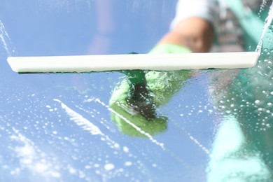 Woman washing window with squeegee tool against blue sky, closeup