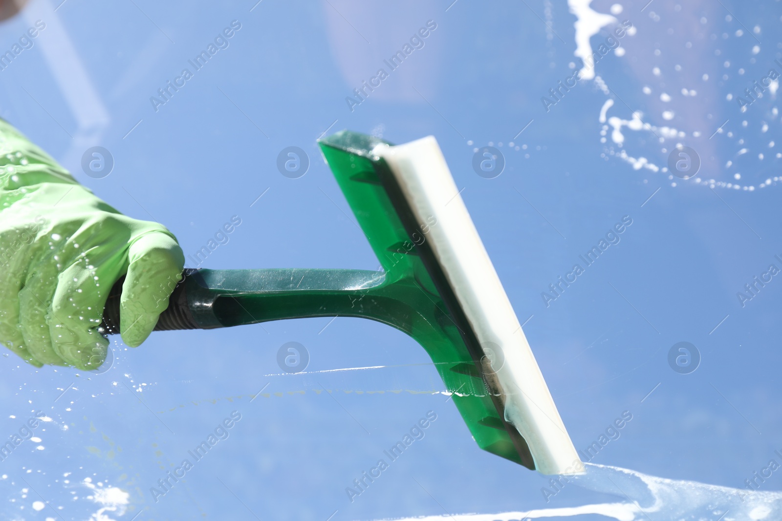 Photo of Woman washing window with squeegee tool against blue sky, closeup