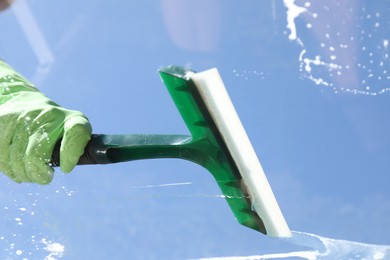 Woman washing window with squeegee tool against blue sky, closeup