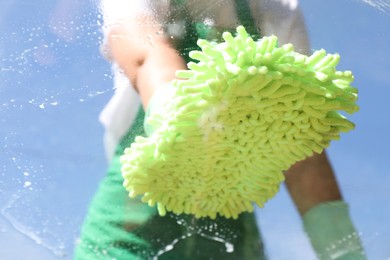 Photo of Woman washing window with microfiber mitt against blue sky, closeup