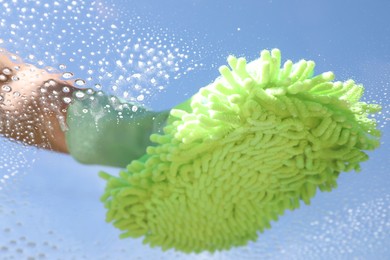 Woman washing window with microfiber mitt against blue sky, closeup