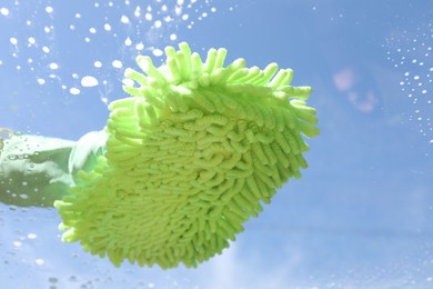 Photo of Woman washing window with microfiber mitt against blue sky, closeup