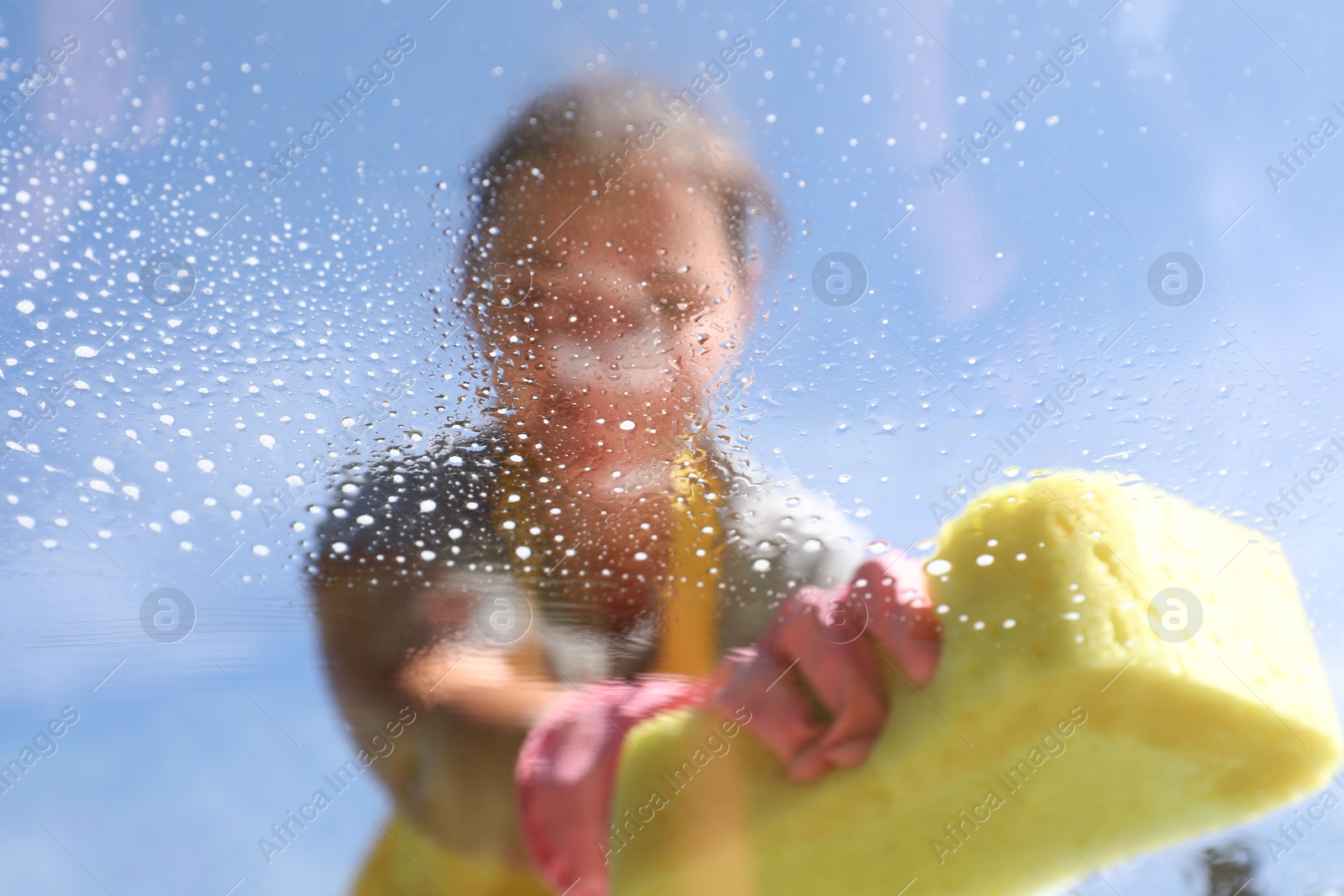 Photo of Woman washing window with sponge against blue sky, closeup