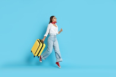 Photo of Happy young woman in sunglasses with suitcase on light blue background, space for text