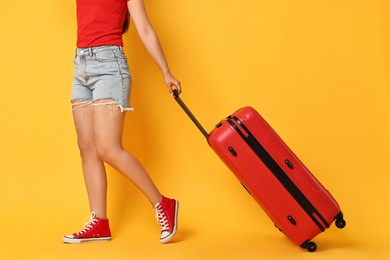 Woman with suitcase on orange background, closeup