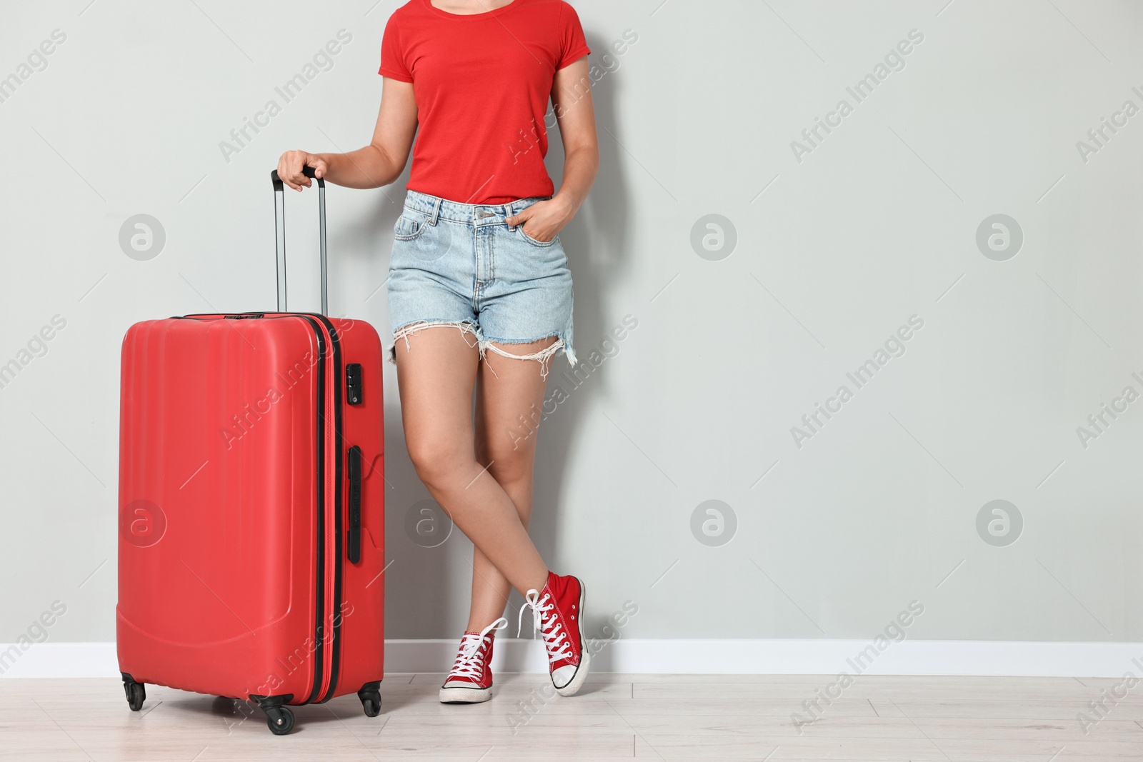 Photo of Woman with suitcase near light gray wall indoors, closeup. Space for text