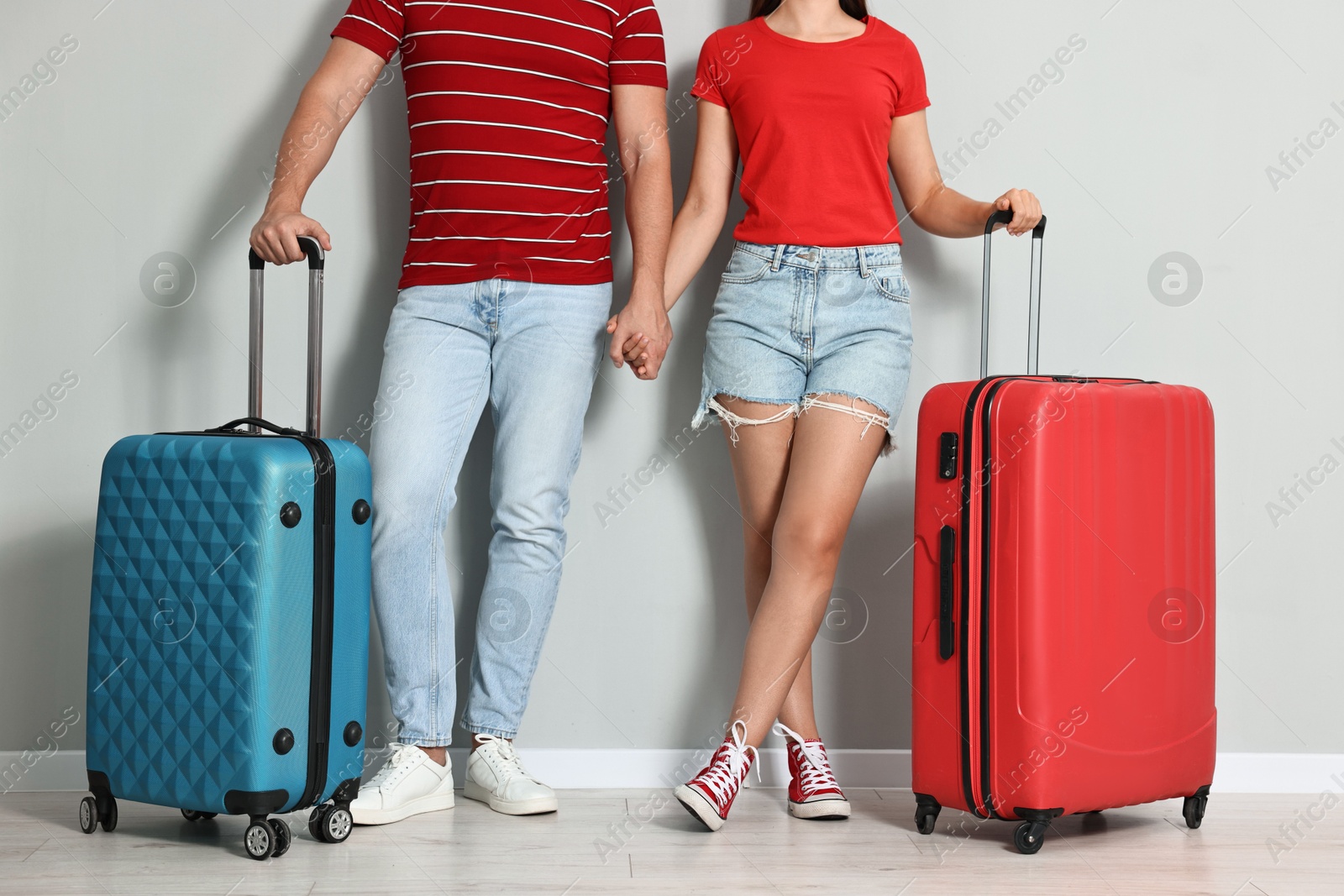 Photo of Man and woman with suitcases near light gray wall indoors, closeup