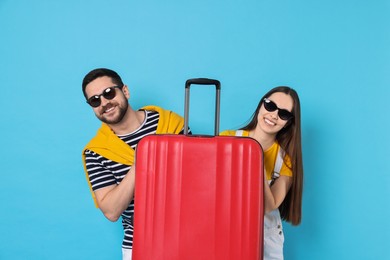 Photo of Happy couple in sunglasses with suitcase on light blue background