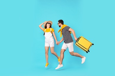 Photo of Happy man with suitcase and woman jumping on light blue background