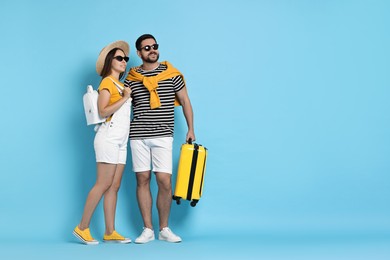 Happy man with suitcase and woman on light blue background, space for text