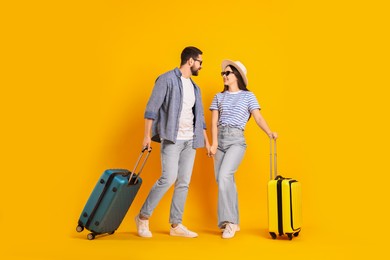 Photo of Happy couple in sunglasses with suitcases on orange background