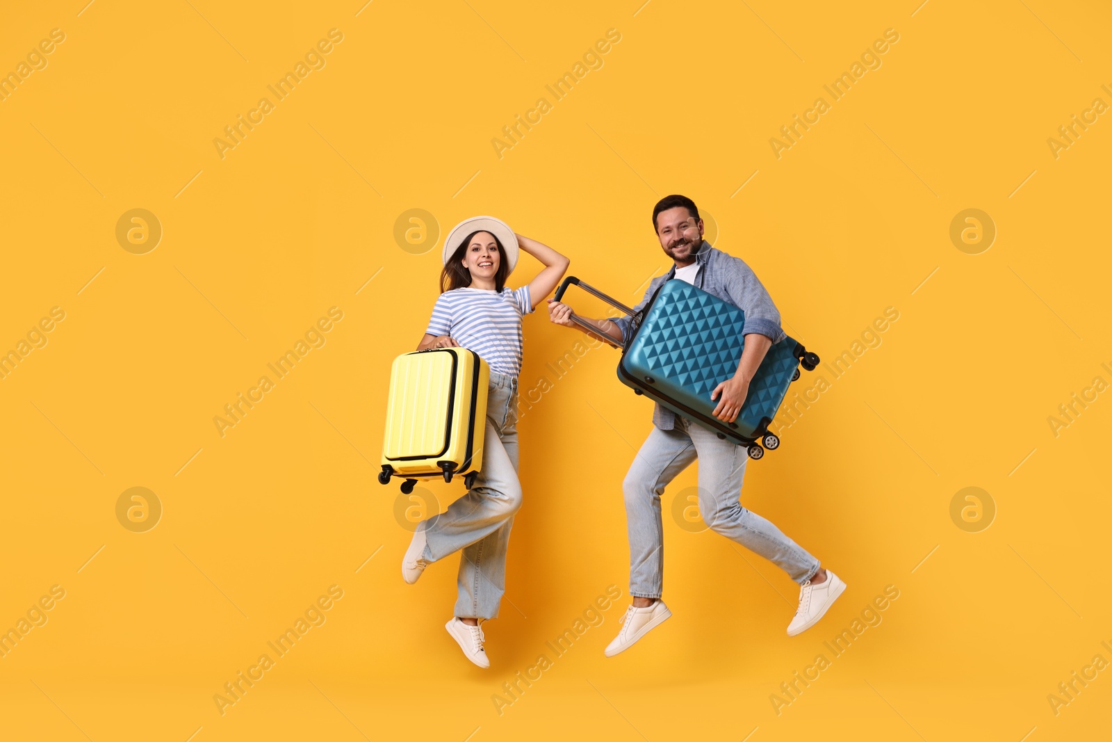 Photo of Happy couple with suitcases jumping on orange background