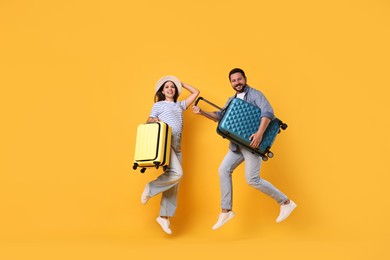 Happy couple with suitcases jumping on orange background