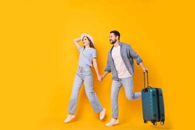 Photo of Happy man with suitcase and woman running on orange background