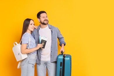 Photo of Happy couple with suitcase, passport and tickets on orange background, space for text