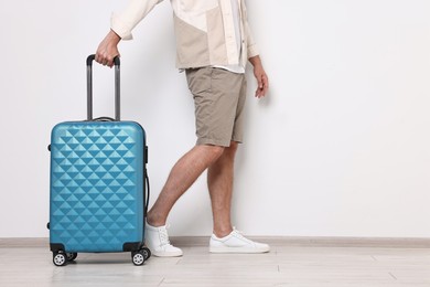 Photo of Man with suitcase near light wall walking indoors, closeup. Space for text