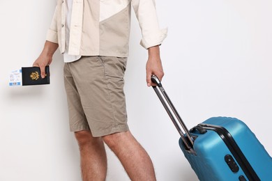 Man with suitcase, passport and ticket on light background, closeup