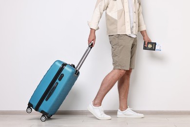 Man with suitcase, passport and ticket walking indoors, closeup