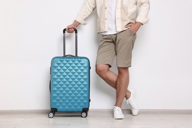 Man with suitcase near light wall indoors, closeup