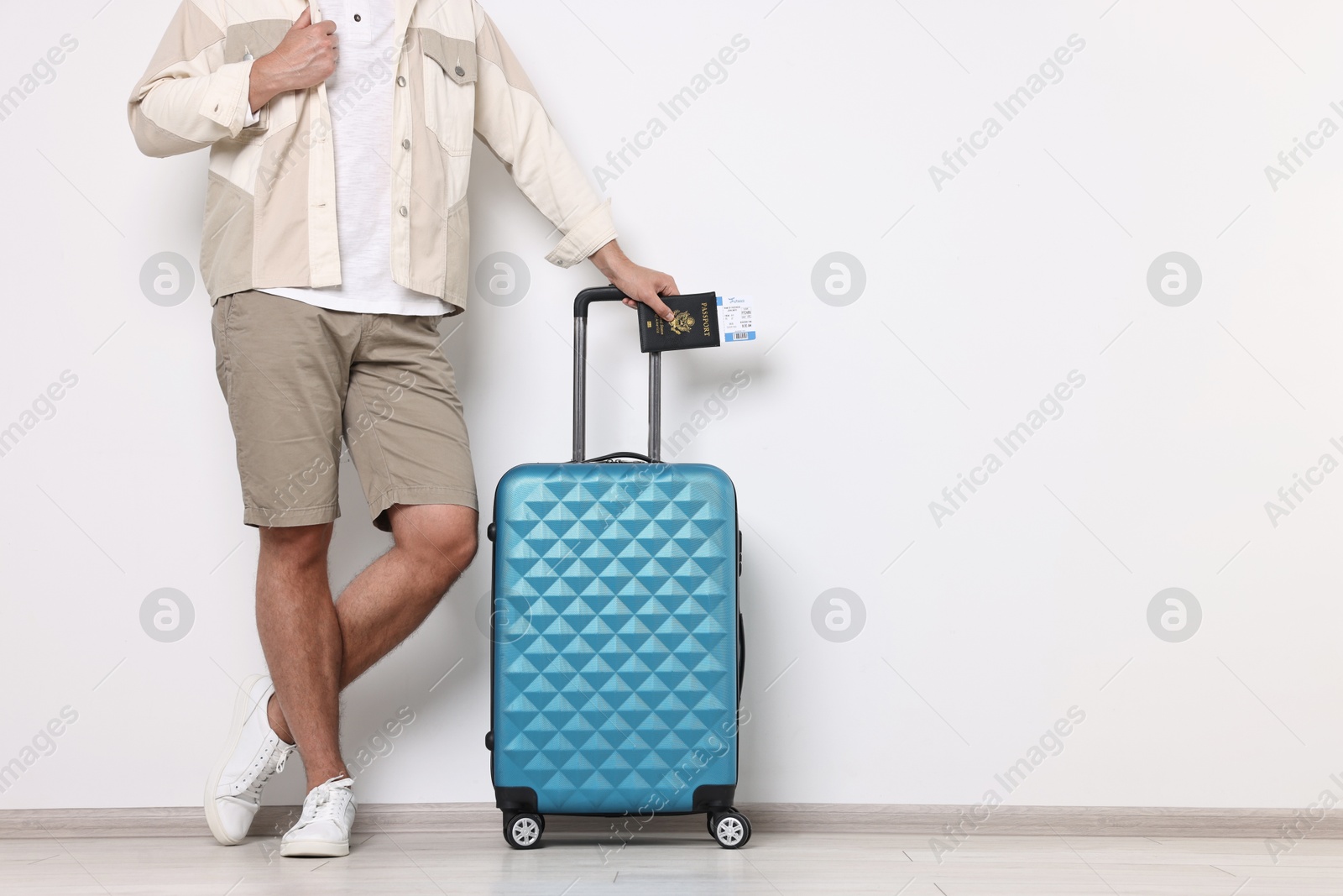 Photo of Man with suitcase, passport and ticket near light wall indoors, closeup. Space for text