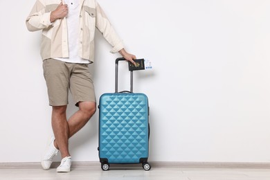 Man with suitcase, passport and ticket near light wall indoors, closeup. Space for text