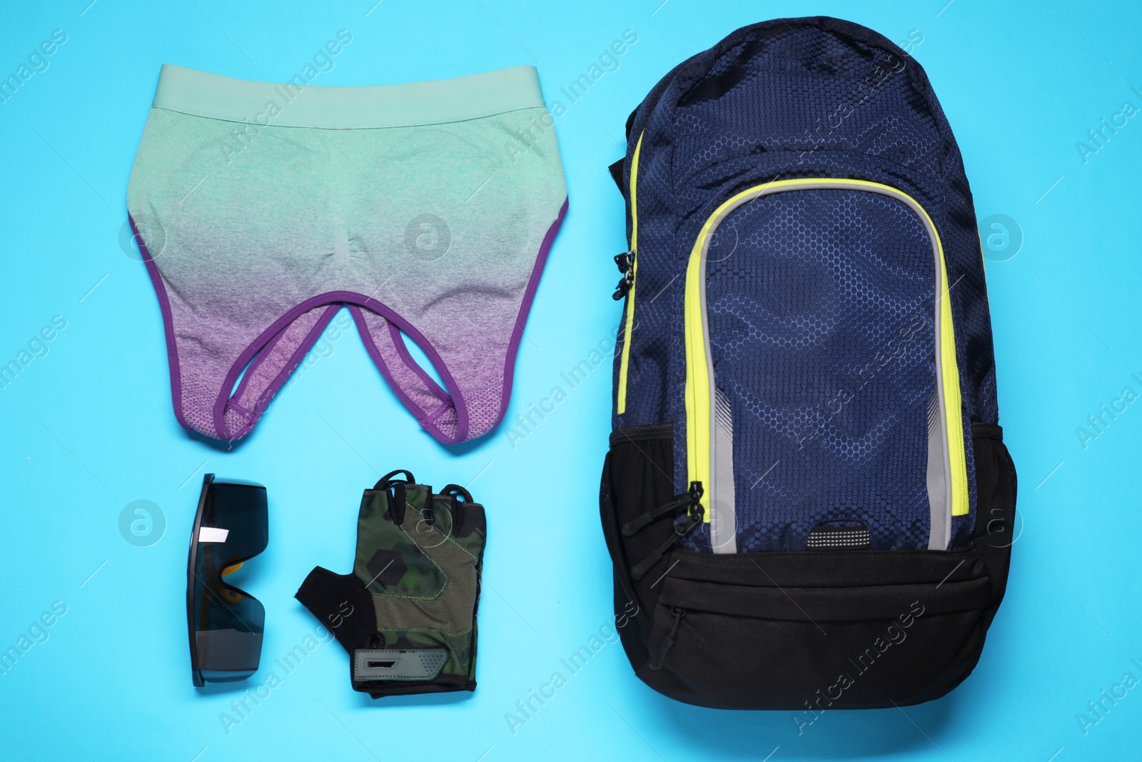 Photo of Backpack, sports bra, fingerless cycling glove and goggles on light blue background, flat lay