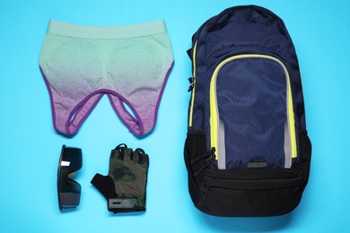 Photo of Backpack, sports bra, fingerless cycling glove and goggles on light blue background, flat lay