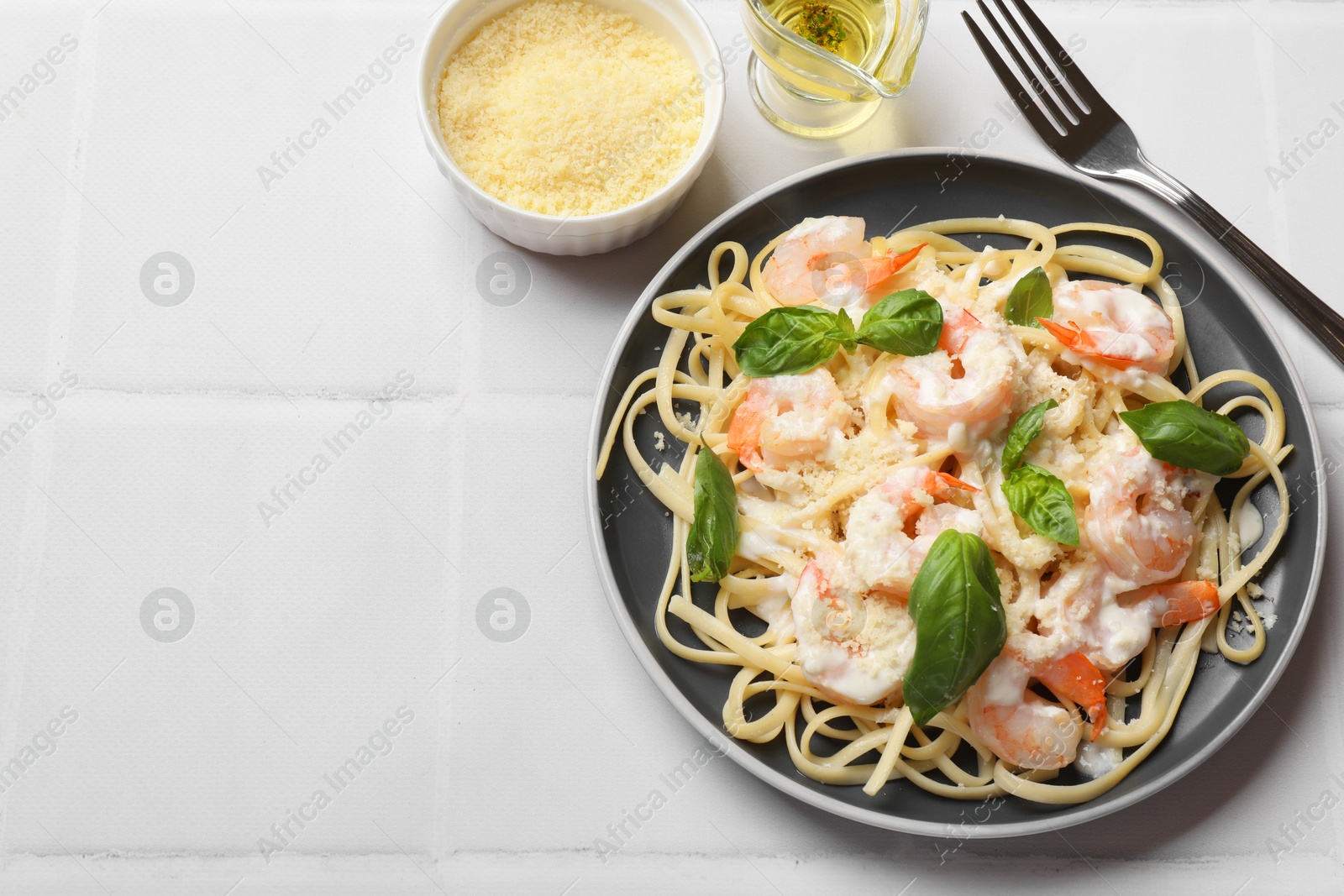 Photo of Tasty pasta with shrimps served on white tiled table, flat lay. Space for text