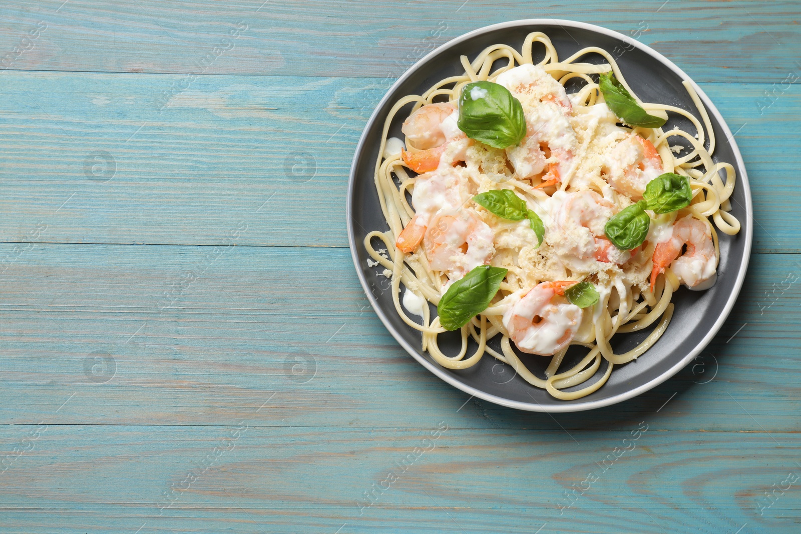 Photo of Tasty pasta with shrimps on light blue wooden table, top view. Space for text