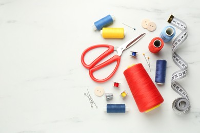 Flat lay composition with different sewing supplies on white marble table. Space for text