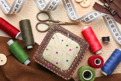 Flat lay composition with different sewing supplies on beige textured table