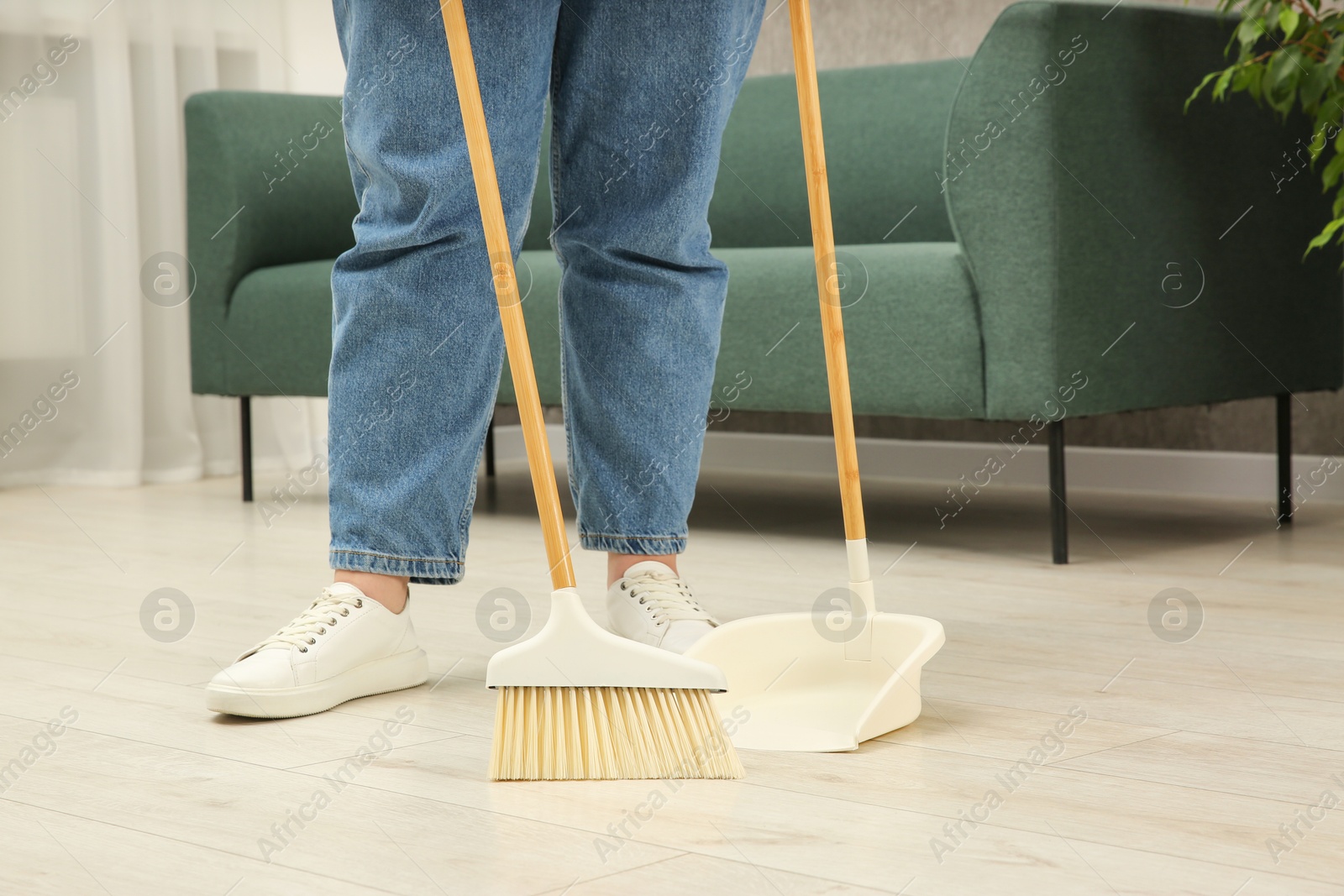 Photo of Woman with broom and dustpan cleaning floor indoors, closeup